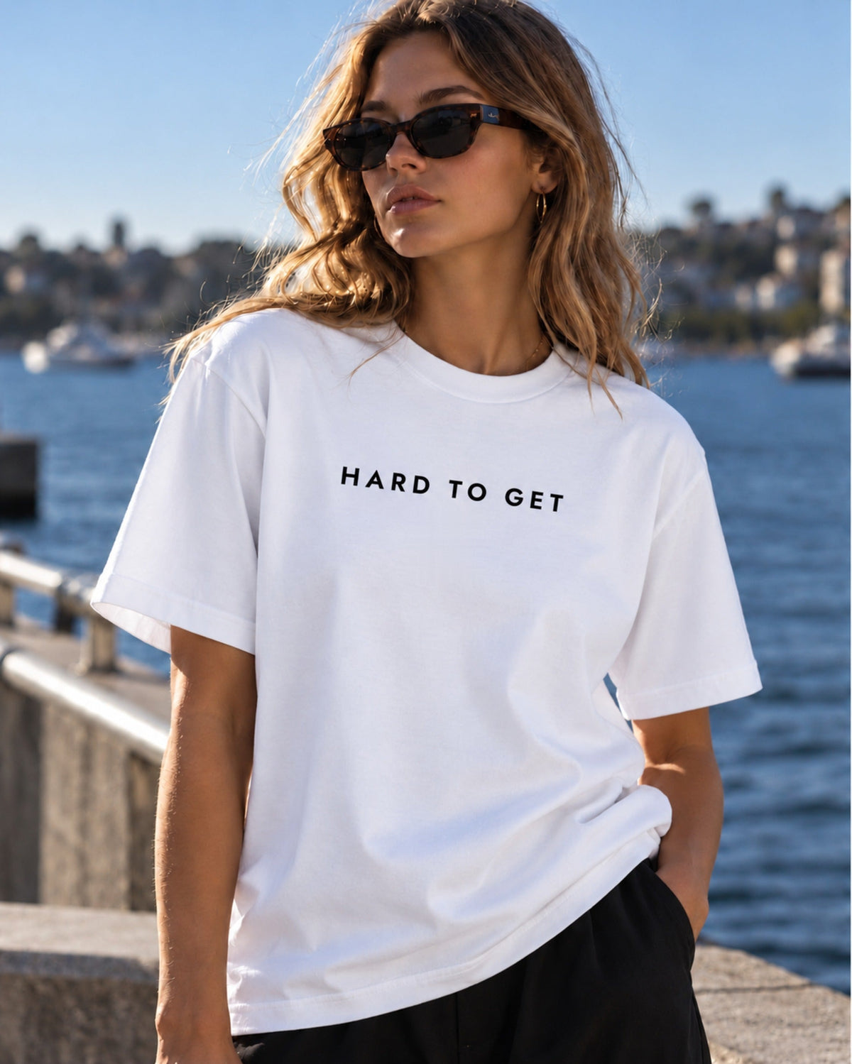 Very Hard to Get tee in White, worn by a model on the harbour (front)